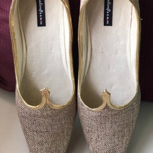 K&ouml;nnte beinhalten: Ein Paar goldene und braune Stoffschuhe mit spitzer Zehenpartie und goldener Verzierung. Die Schuhe haben den Text "handicrafts in me" auf der Innenseite.