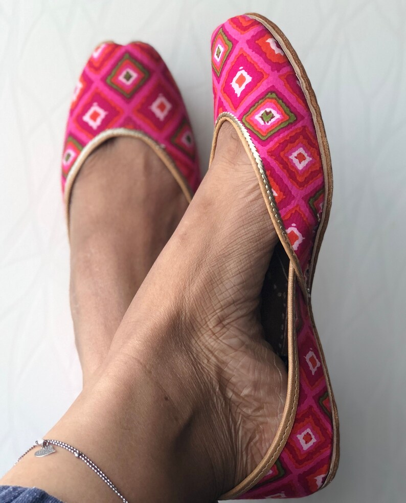 May include: A pair of pink and green flat shoes with a geometric pattern. The shoes have a pointed toe and a low heel.
