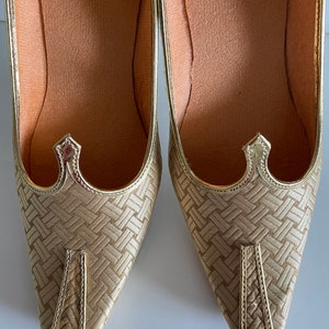 May include: A pair of gold woven pointed-toe shoes with a decorative detail at the top of the vamp.