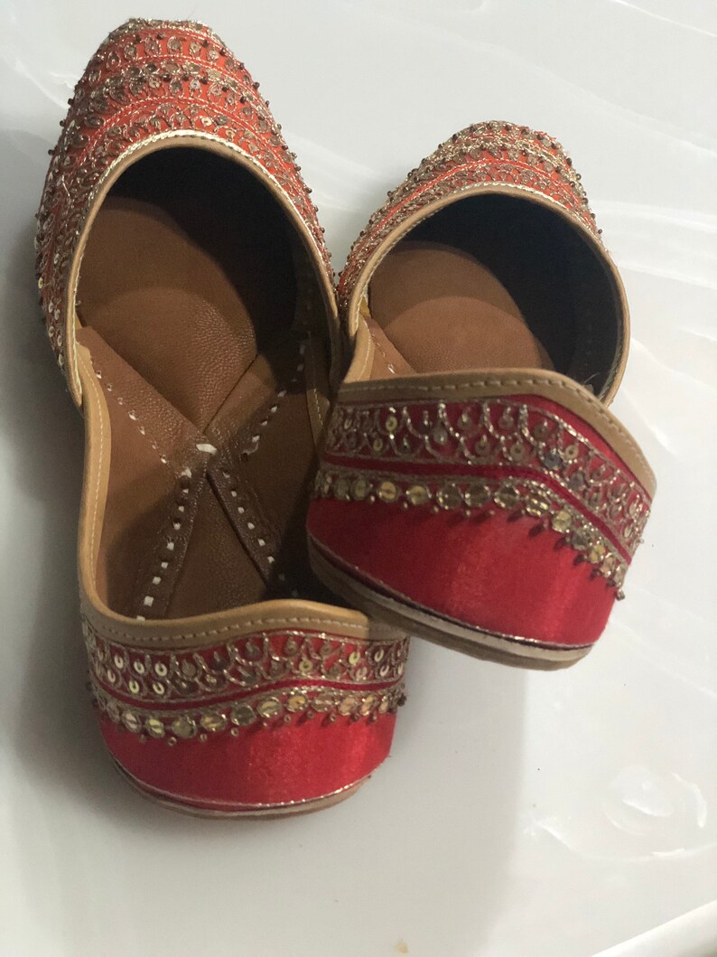 May include: A pair of red embroidered flat shoes with gold and silver embellishments. The shoes have a pointed toe and a low heel.