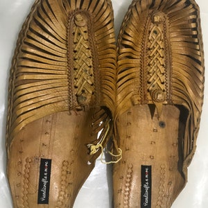 May include: A pair of tan leather sandals with a woven design. The sandals have a label that says "handicrafts n more".