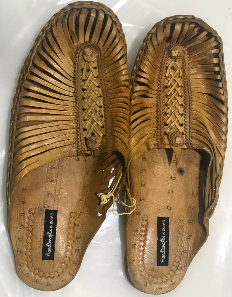 May include: A pair of tan leather sandals with a woven design. The sandals have a label that says "handicrafts n more".