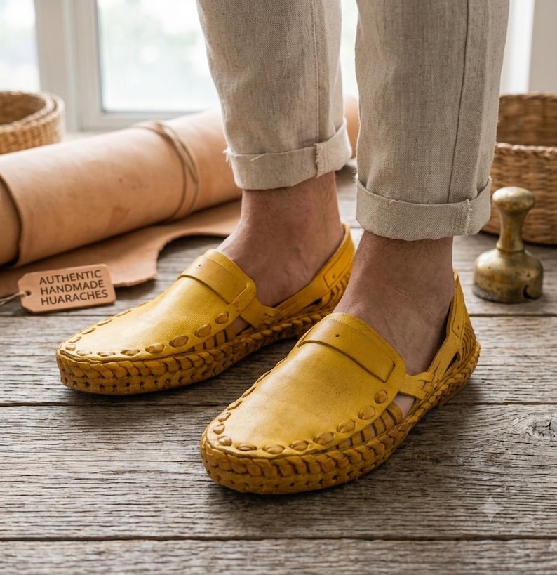 May include: A pair of yellow leather huarache sandals featuring a woven design along the edges and a strap across the top. A small rectangular tag with the text AUTHENTIC HANDMADE HUARACHES is visible next to the footwear on a wooden surface.