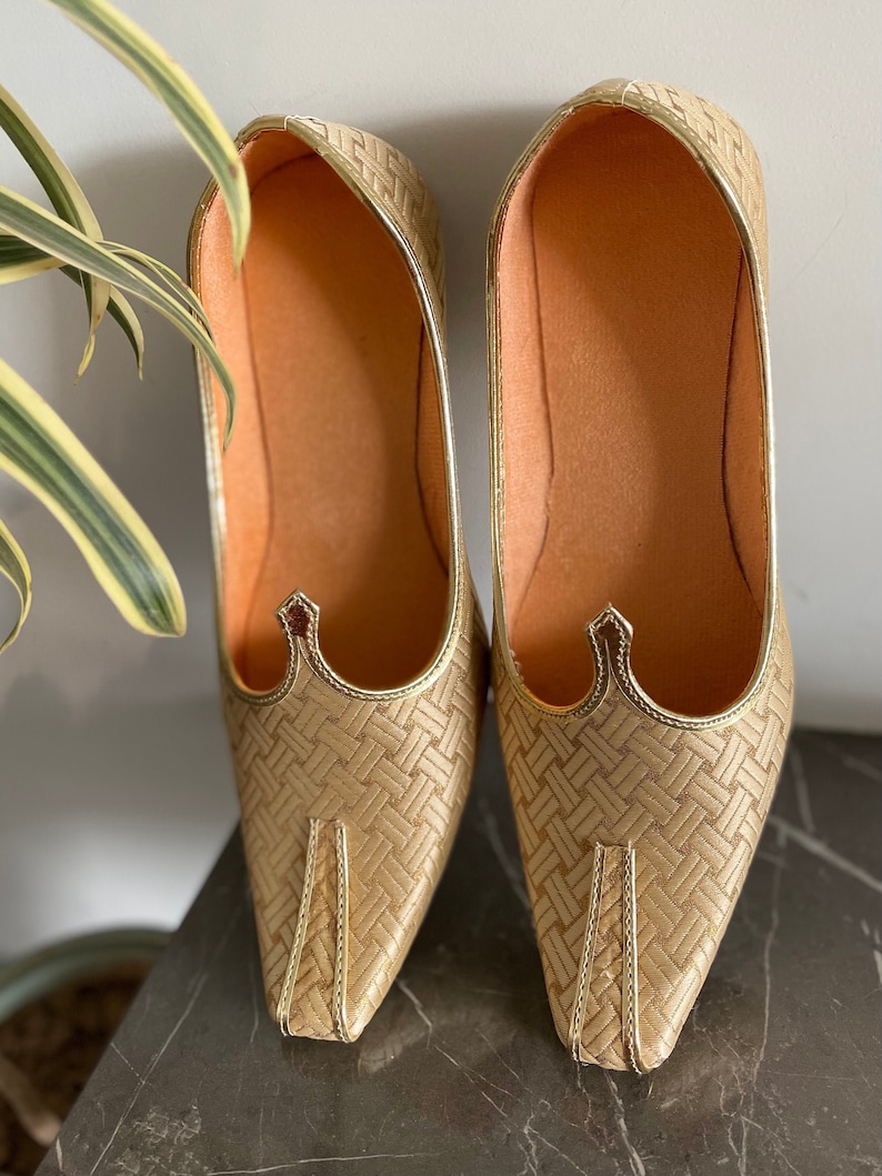May include: A pair of gold woven pointed-toe flat shoes with a decorative detail on the top.