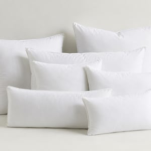 May include: A collection of seven white pillows in various rectangular and square sizes. The pillows are arranged in a layered group, featuring smooth, plain white fabric covers and soft, plump forms with visible seams along the edges.