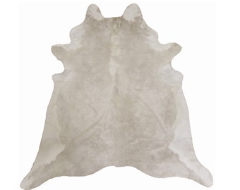 May include: A light gray cowhide rug with a natural, slightly distressed look. The rug is soft and fluffy, with a natural, organic feel.