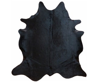 May include: A solid black cowhide rug with an irregular shape. The rug has a soft, textured appearance and is likely made of genuine leather. The rug is designed to be placed on the floor as a decorative element.