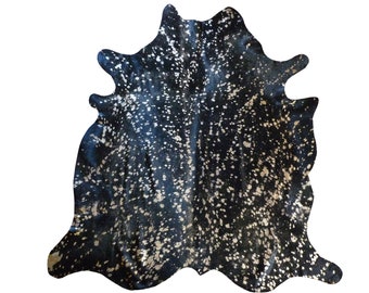 May include: Black cowhide rug with gold metallic spots. The rug has a natural, irregular shape.
