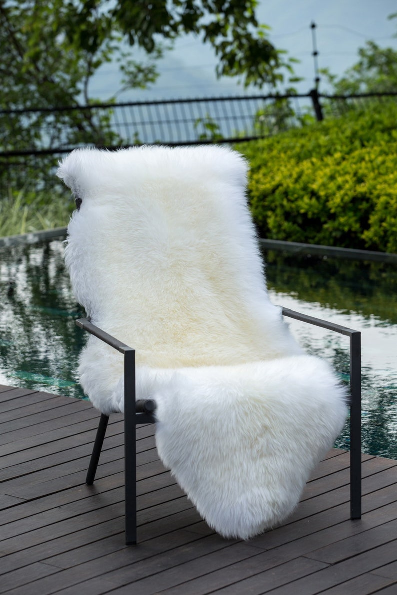 May include: A white sheepskin rug draped over a black metal chair. The chair is on a wooden deck next to a swimming pool.