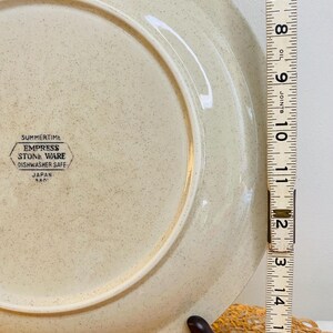 May include: A beige Empress Stone Ware plate with a speckled design. The plate is approximately 30 cm in diameter. The plate has the text "SUMMERTIME EMPRESS STONE WARE DISHWASHER SAFE JAPAN" printed on the back.