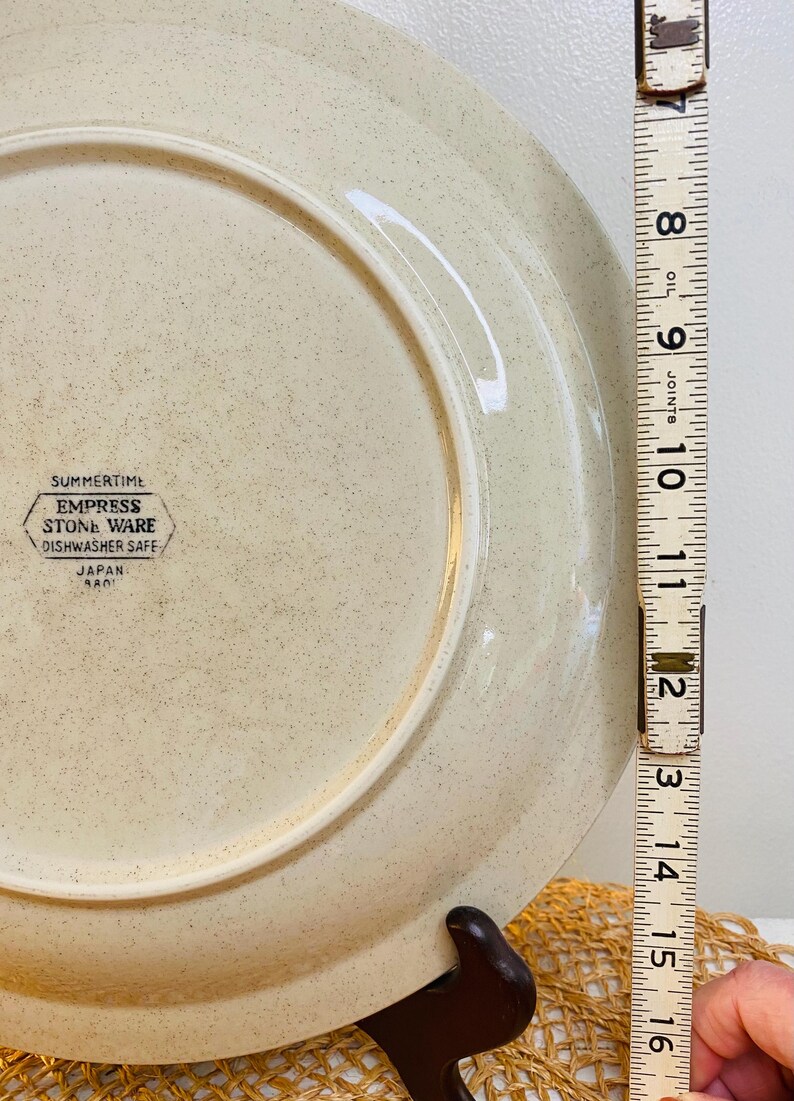 May include: A beige Empress Stone Ware plate with a speckled design. The plate is approximately 30 cm in diameter. The plate has the text "SUMMERTIME EMPRESS STONE WARE DISHWASHER SAFE JAPAN" printed on the back.