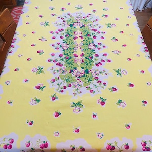 May include: A rectangular tablecloth with a bright yellow background featuring a central vertical pattern of green leaves and pink strawberry blossoms. The fabric is scattered with small individual strawberry motifs and has a border of strawberries.