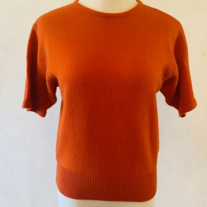 May include: A short-sleeved, rust-colored sweater on a white mannequin.