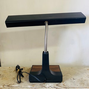 May include: A black desk lamp with a flexible gooseneck and a rectangular light fixture. The lamp has a wood-grain base.