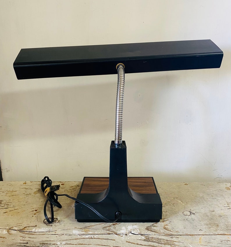 May include: A black desk lamp with a flexible gooseneck and a rectangular light fixture. The lamp has a wood-grain base.
