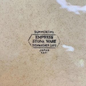 May include: A speckled, cream-coloured plate featuring the text "SUMMERTIME" above a hexagonal emblem that reads "EMPRESS STONE WARE DISHWASHER SAFE" and "JAPAN 8801".