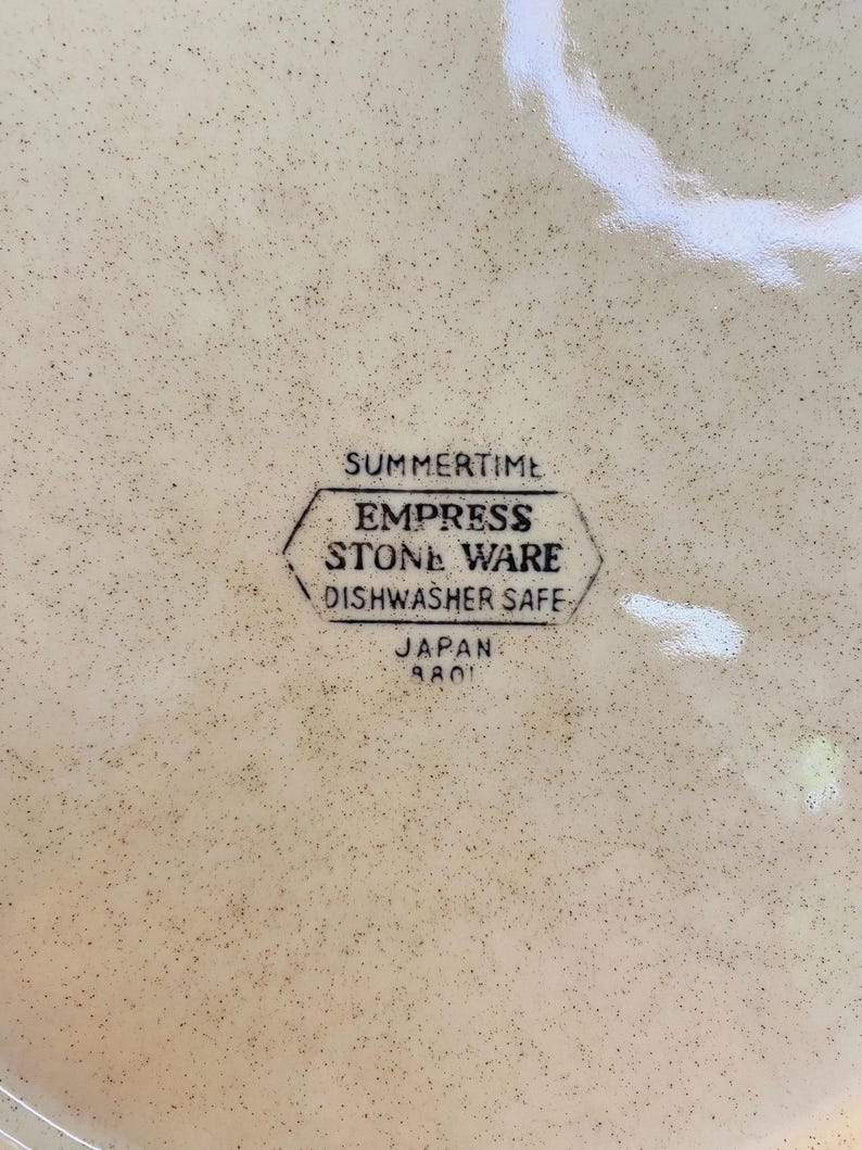 May include: A speckled, cream-coloured plate featuring the text "SUMMERTIME" above a hexagonal emblem that reads "EMPRESS STONE WARE DISHWASHER SAFE" and "JAPAN 8801".