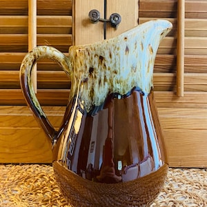 May include: A brown and white glazed ceramic pitcher with a wide mouth and a handle. The pitcher has a mottled brown and white glaze with a brown base.