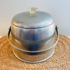 May include: Silver aluminum ice bucket with a clear plastic lid and a handle. The bucket is sitting on a woven straw mat.