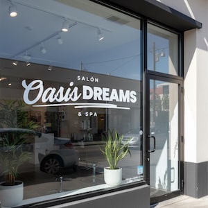 May include: Exterior view of a salon and spa with large glass windows and a black door frame. The business name, "Oasis Dreams & Spa," is displayed in white lettering on the glass. Potted plants are visible inside and outside the salon.