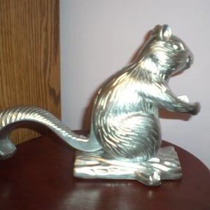 May include: Silver squirrel nutcracker with a detailed, textured finish. The squirrel is sitting on a base with a textured wood grain design.