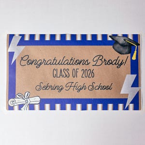 May include: A graduation card with a brown background and blue border. The card says "Congratulations Brody! CLASS OF 2026 Sebring High School". It features a graduation cap, lightning bolts, and a diploma illustration.