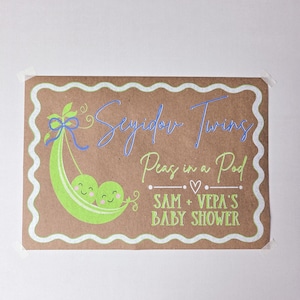 May include: A rectangular sign with a brown background and a white wavy border. The sign features a green pea pod with two smiling peas and the text "Seyidov Twins Peas in a Pod SAM + VEPA'S BABY SHOWER" in blue and green.