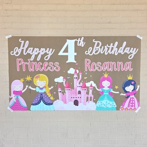 May include: A large brown banner with the text "Happy 4th Birthday Princess Rosanna" in white and pink script. Four princess illustrations and a pink castle are featured below the text. The banner is taped to a brick wall.
