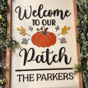 Puede incluir: Cartel enmarcado en madera con las palabras "Welcome to Our Patch" y "The Parkers" en escritura negra. Una gran calabaza naranja y hojas de otoño decoran el cartel. El fondo es de color crema.