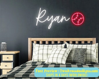 Könnte beinhalten: Ein wandmontiertes Neonschild, das den Namen Ryan in weißer Schreibschrift neben einer roten, kreisförmigen Baseball-Grafik mit weißen Nahtdetails zeigt, angebracht über einem hölzernen Bettrahmen mit karierter Bettwäsche.