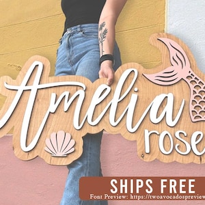 May include: A wooden sign with the name "Amelia rose" in white script. The sign is decorated with a pink mermaid tail and a pink seashell.