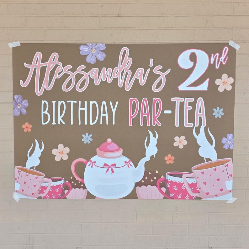 May include: A brown poster with the text "Alessandra's 2nd BIRTHDAY PAR-TEA" in pink and white. The poster features illustrations of teacups, a teapot, and flowers in pink, white, and peach colors. The poster is taped to a brick wall.