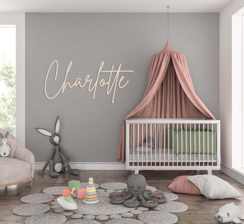 May include: A nursery room featuring a white crib with a dusty pink canopy, a wooden wall sign reading Charlotte in cursive script, a gray rabbit plush, a gray octopus plush, a pastel stacking ring toy, and a gray circular petal-patterned rug.