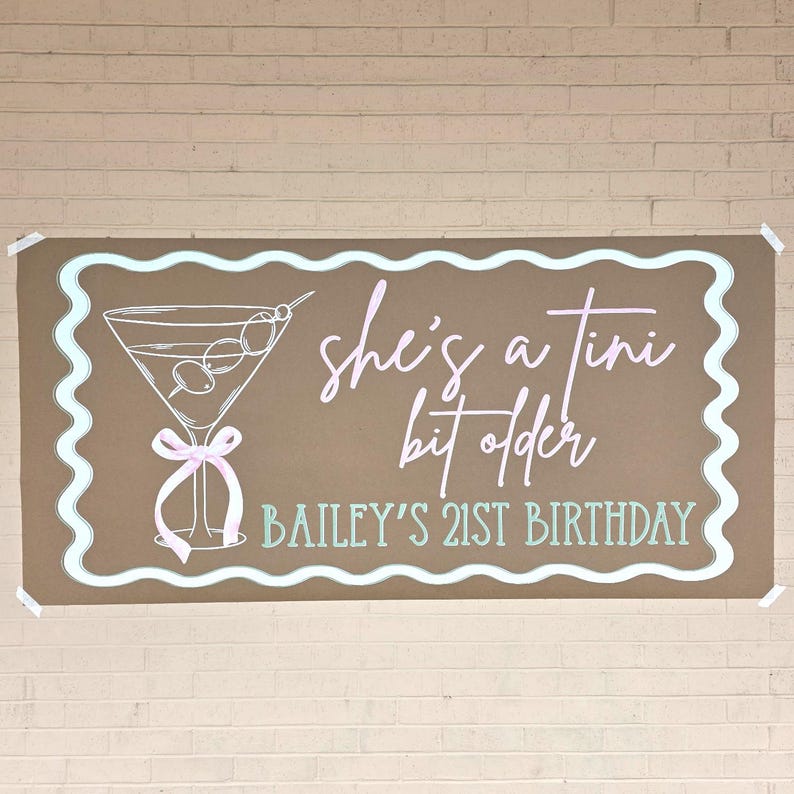 May include: A brown banner with a light blue wavy border and the text "she's a tini bit older" in pink script. A martini glass illustration is on the left. The text "BAILEY'S 21ST BIRTHDAY" is at the bottom.