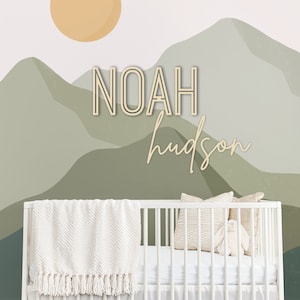 Pode incluir: Um ber&ccedil;o branco com um cobertor branco e um travesseiro branco com um padr&atilde;o de listras marrons e brancas. O ber&ccedil;o est&aacute; em frente a uma parede com um mural de montanha verde e branca e o nome "NOAH hudson" escrito em marrom.