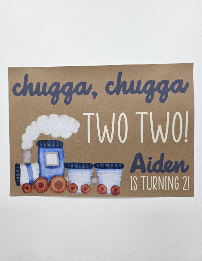 May include: A brown card with a watercolor illustration of a blue train with the text "chugga, chugga TWO TWO! Aiden IS TURNING 2!". The train has brown wheels and a white cloud of smoke.