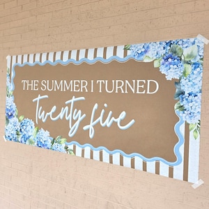 May include: A rectangular banner with the text "THE SUMMER I TURNED Twenty five" in white and light blue script. The banner has a brown background with a light blue scalloped border and blue and white striped edges. Blue hydrangea flowers decorate the corners.