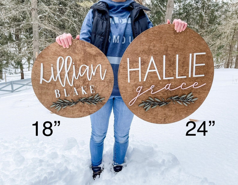 Op de afbeelding: Twee ronde houten borden met namen en groen. Het grotere bord is 24 inch in diameter en heeft de tekst "Hallie grace" in witte en roze letters. Het kleinere bord is 18 inch in diameter en heeft de tekst "Lillian Blake" in witte letters.