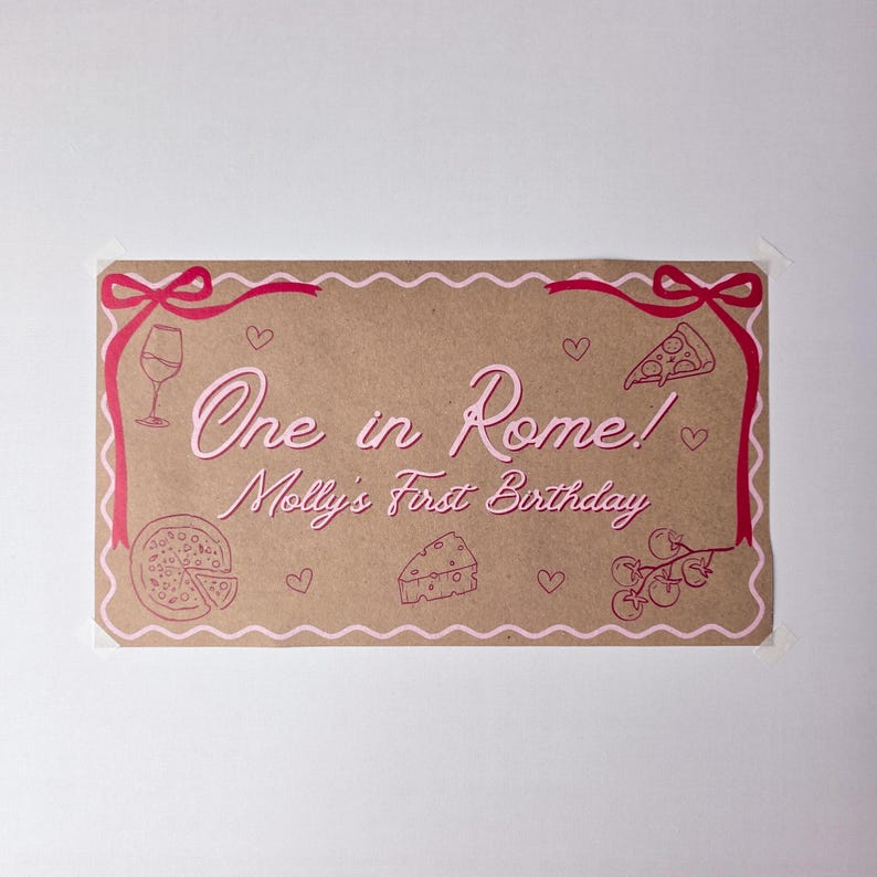 May include: A rectangular brown paper sign with a scalloped pink border and red ribbon accents at the top corners. The text reads One in Rome! Molly's First Birthday in pink. Illustrations include a wine glass, pizza slice, whole pizza, cheese, and tomatoes.