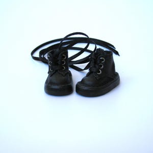 May include: A pair of miniature black leather boots with matching laces. The boots have a classic lace-up design with silver-colored eyelets. The boots are set against a white background.
