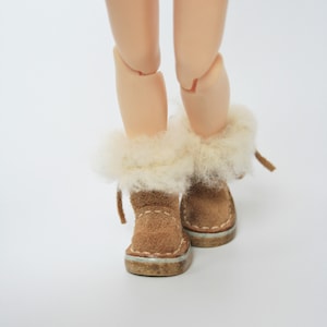 May include: A pair of brown suede boots with white faux fur trim. The boots have a light brown sole and are tied with a white string.
