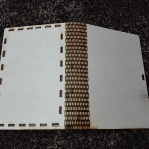 Peut inclure: Un livre en bois blanc avec une reliure &agrave; motifs marrons. Le livre est ferm&eacute; et a une couverture blanche.
