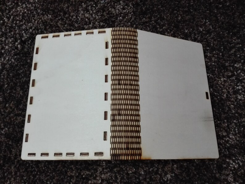 Peut inclure: Un livre en bois blanc avec une reliure &agrave; motifs marrons. Le livre est ferm&eacute; et a une couverture blanche.
