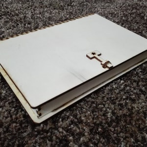 Könnte beinhalten: Ein weißes Holzjournal mit einem Holzkreuz-Design auf dem vorderen Umschlag. Das Journal hat eine Spiralbindung und ist geschlossen.