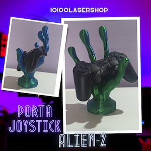 Könnte beinhalten: Eine grüne und blaue Alien-Hand hält einen schwarzen Sony PlayStation-Controller. Die Hand hält den Controller in die Luft. Der Text "PORTA JOYSTICK ALIEN-2" steht unter dem Bild.