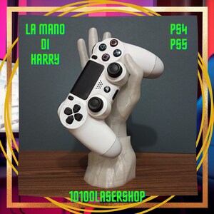 Op de afbeelding: Een witte PlayStation-controller wordt vastgehouden door een 3D-geprinte hand. De hand houdt de controller vast op een manier die een persoon nabootst die een videogame speelt. De basis van de hand is een 3D-geprinte standaard. De tekst "LA MANO DI HARRY" is zichtbaar in de linkerbovenhoek van de afbeelding. De tekst "PS4 PS5" is zichtbaar in de rechterbovenhoek van de afbeelding. De tekst "10100LASERSHOP" is zichtbaar in het midden onderaan de afbeelding.