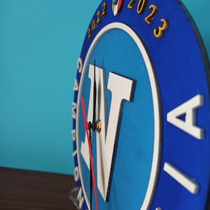 May include: A blue and white wooden clock with the text "2022 2023" and the letter "N". The clock hands are black and red. The clock is round and has a white border.