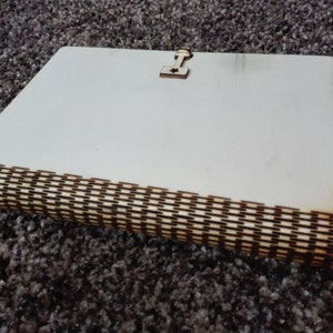 Peut inclure: Un journal en bois blanc avec une incrustation d&eacute;corative en bois sur le bord. Le journal a un petit fermoir en bois sur le devant.