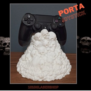 Op de afbeelding: Een witte schedelvormige standaard voor een zwarte PlayStation 4-controller. De standaard is gemaakt van 3D-geprint plastic en heeft een stapel schedels. De tekst "PORTA JOYSTICK" is zichtbaar in de rechterbovenhoek van de afbeelding.