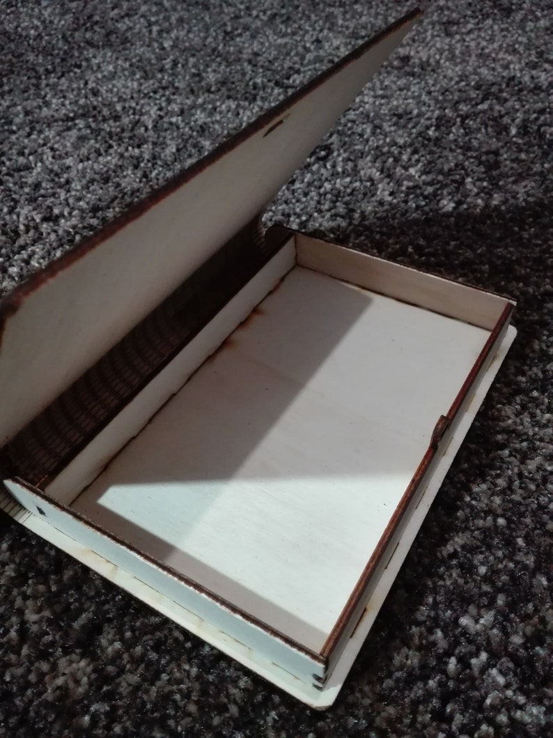 Peut inclure: Une bo&icirc;te en bois avec un couvercle &agrave; charni&egrave;re, ouverte pour r&eacute;v&eacute;ler un int&eacute;rieur vide. La bo&icirc;te est en bois brun clair avec une teinture brun fonc&eacute;.